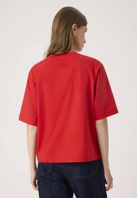 Piros pamut póló, kerek nyakkivágással és laza szabással. Rövid ujjú, és kis emelt logó részlet található a hátsó részen. Kényelmes dizájn.