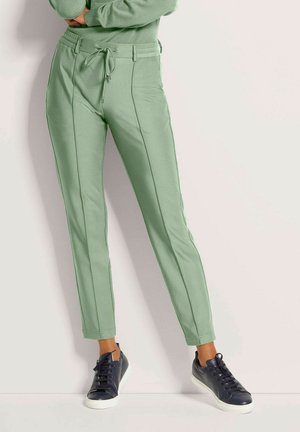Lichtgroene tapered broek met een trekkoord in de taille, met contrasterende zijnaad en gecombineerd met donkerblauwe sneakers. Het stof heeft een gladde textuur.