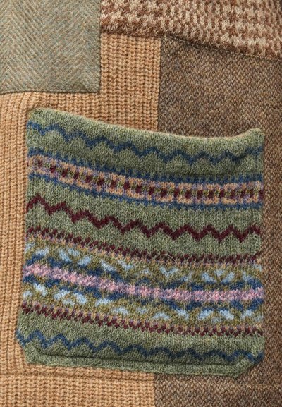 Têxtil verde tricotado com padrões em ziguezague azul, rosa e bordô. Rodeado por vários pedaços de tecido castanho texturizado em disposição de colcha de retalhos.
