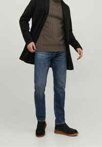 Czarny płaszcz, ciemnoszary sweter w warkocze, niebieskie dżinsy i czarne buty z brązowymi podeszwami. Swobodny, warstwowy strój z teksturowymi elementami.