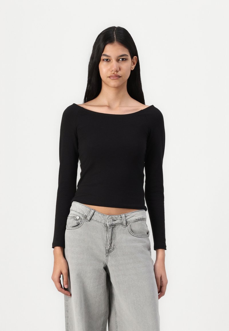 Black, long-sleeve crop top with an off-the-shoulder neckline. Paired with light gray, wide-leg jeans featuring a button and zip closure.