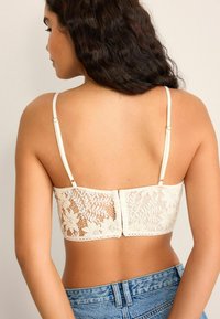Crèmekleurige kanten bralette met bloemmotieven, verstelbare bandjes en een zachte achtersluiting. Gepaarde met high-waisted denim shorts.