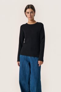 Pulover lung negru cu maneci lungi, realizat dintr-un material tricotat moale, asortat cu pantaloni din denim albastru, cu talie largă. Guler simplu de tip crew și siluetă ajustată în zona bustului.