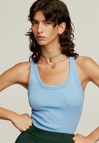 Top de tirantes acanalado en azul claro con escote redondeado, combinado con collares en capas y pantalones de tiro alto verdes.