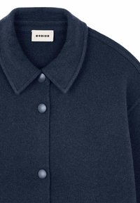 Navyblauwe gebreide shirtjack met een ronde kraag, vijf knoopsluitingen, ribbeltextuur en een label met de tekst "RODIER."