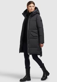 Lang sort puffet frakke med høj krave, lynlåslukning og store frontlommer. Har en quiltet design og tykt materiale, ideelt til varme.