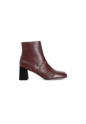 Stivaletto in pelle bordeaux con tacco spesso nero e dettaglio decorativo a fibbia. Presenta una punta affusolata e una texture liscia.