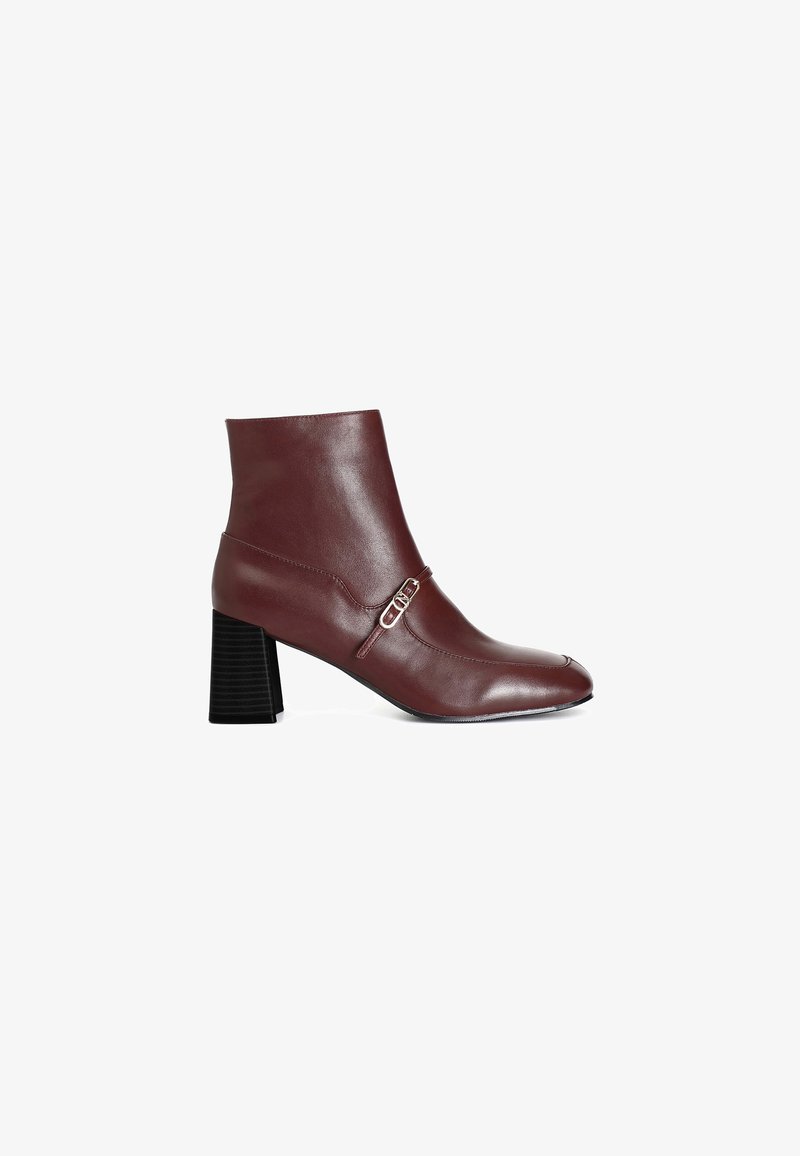 Stivaletto in pelle bordeaux con tacco spesso nero e dettaglio decorativo a fibbia. Presenta una punta affusolata e una texture liscia.