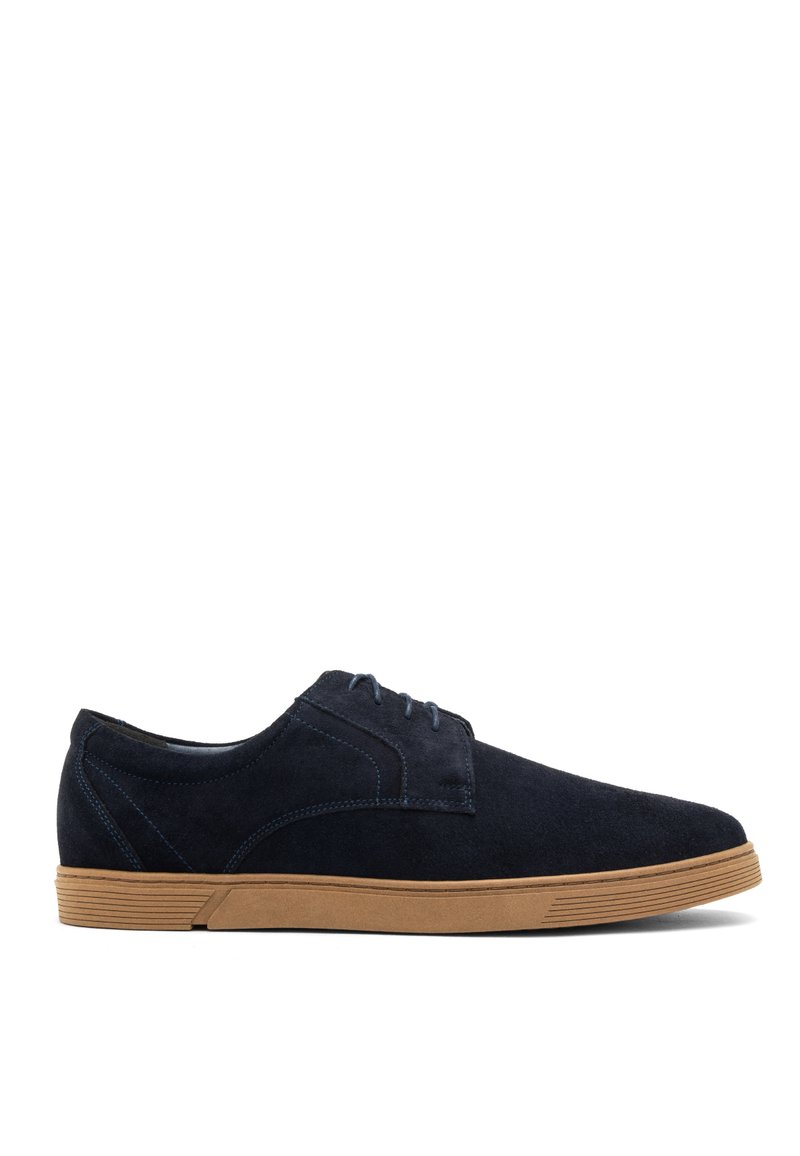 Zapatos de ante azul marino con una textura suave, un diseño de cordones y una suela de goma marrón claro con ranuras horizontales.