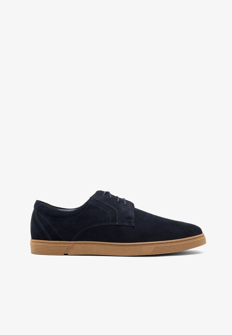 Zapatos de ante azul marino con una textura suave, un diseño de cordones y una suela de goma marrón claro con ranuras horizontales.