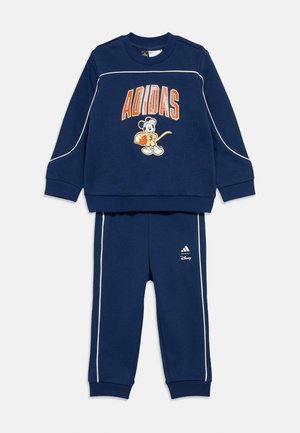 Temno modra trenirka sestavljena iz puloverja s potiskom Mickey Mouse in napisom "ADIDAS"; vključuje ujemajoče se hlače z belimi dodatki in logotipom.