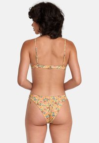 Floral bikini in yellow with multicolor pattern. Adjustable straps and a clasp at the back. Material appears smooth with a moderate cut.