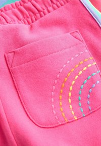 Rozā sporta bikses ar savāktu jostasvietu un aizmugurējo kabatu, kas rotāta ar daudzkrāsainiem izšūtiem arkiem dzeltenā, rozā un zila krāsā.