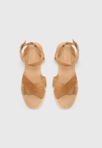 Brune semskede sandaler med krydsseler, en spændeankelrem og en tekstureret beige sål med syede detaljer.