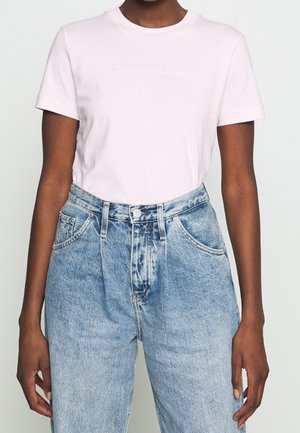 Person iført en hvid Calvin Klein Jeans t-shirt, stukket ned i højhøj tallige lyseblå denimjeans med frontlommer.