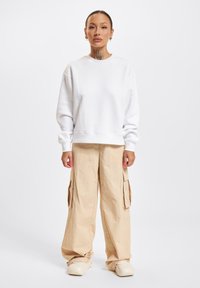 Weißes Sweatshirt mit Rundhalsausschnitt, kombiniert mit lockeren beigen Cargo-Hosen mit Seitentaschen. Das Outfit hat eine entspannte Passform und eine weiche Textur.