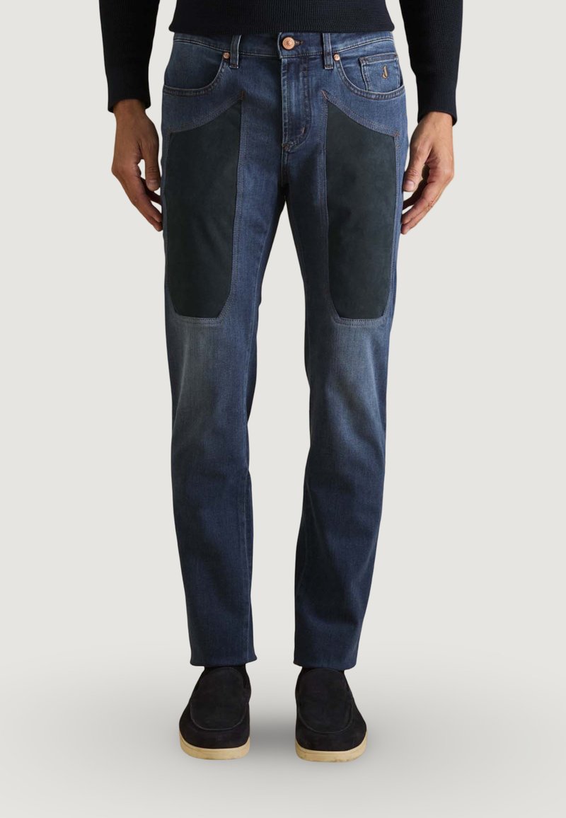 Jean bleu foncé avec des patchs en suede noir contrastants sur les cuisses, coupe slim, design classique à cinq poches, et accents en cuivre.