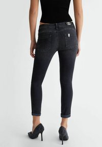 Jeans ajustados de mezclilla oscura con una cintura media, que cuentan con dobladillos enrollados, dos bolsillos traseros y una pequeña etiqueta de la marca encima del bolsillo derecho.