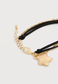 Γοητεία χρυσού αστεριού σε βραχιόλι από μαύρο σουέντ και χρυσή αλυσίδα με κούμπωμα λοβού και ρυθμιζόμενους κρίκους αλυσίδας σε λευκό φόντο.