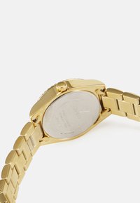 Goldfarbene Uhr mit rundem Gehäuse, Metallarmband, strukturiertem Kronenpaar und glattem silbernen Rücken. Merkmale ein poliertes Finish und ein Gliederdesign.