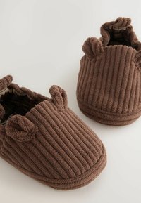 Bruna ribbade tofflor med rundade tår, som har björonöron och en mjuk textur, fodrade med ett mörkt rutig mönster. Ingen synlig hårdvara.