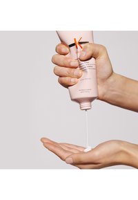 Roze tube van haarproduct die wordt geknepen, waardoor een romige witte substantie in een open hand komt. Rond gevormd, gelabelde voorkant, gladde textuur.