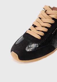 Czarne sneakersy z zamszowej cholewki z błyszczącym akcentem w fakturze krokodyla, beżowymi sznurówkami i tanową gumową podeszwą. Złota marka po boku.