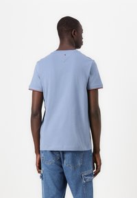 Light blue cotton t-shirt with short sleeves, featuring red and white striped ribbed cuffs and a v-shaped detail at the back.