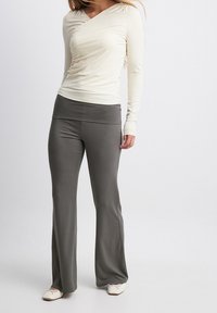 Långärmad krämfärgad topp med en omslagsdesign, parat med grå vida byxor med bred midjeband. Slät textur, mångsidig för aktiv klädsel.
