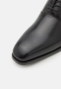 Czarne skórzane buty na formalne okazje z gładkim, zaokrąglonym noskiem, gładką teksturą i minimalnym szwem. Posiada dopasowane sznurowadła i elegancki kształt.