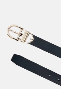 Narrow black leather belt featuring a shiny gold metal buckle with a unique shape. The belt has several adjustment holes along its length.