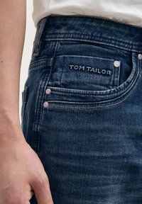Tamno plave traperice s strukturiranim krojem, uključujući stražnji džep s vezom "TOM TAILOR" i srebrnim detaljima.