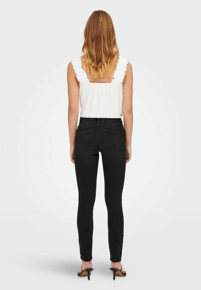 Haut blanc sans manches avec des bretelles froncées, associé à un jean skinny noir taille haute et des sandales à talons noires, vu de dos.