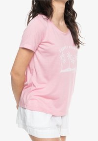 Lyserød t-shirt med korte ærmer, rund halsudskæring og hvid palmetræ grafik. Blødt stof med en afslappet pasform. Bæres med hvide shorts.
