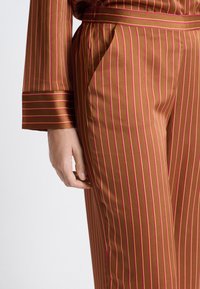 Bruin gestreepte broek met smalle roze lijnen, gemaakt van gladde stof. Heeft een zijzak en een riem in de taille.