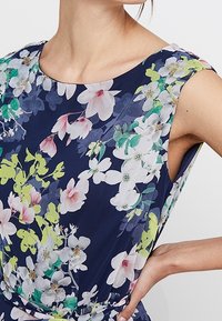 Blommig klänning med marin bakgrund, prydd med livfulla vita, rosa och gröna blommor. Ärmlös design med rundad halsringning och mjukt tyg.