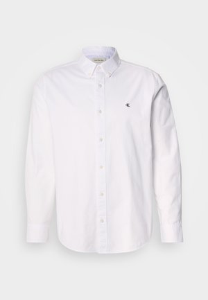 White button-up shirt made of cotton, featuring a classic collar, long sleeves, and a small CK logo on the left chest. Smooth texture.