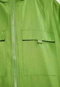 Grøn zip-jakke lavet af glat, let materiale. Har to frontlommer, tekstureret overflade og matchende lynlåsdetalje.