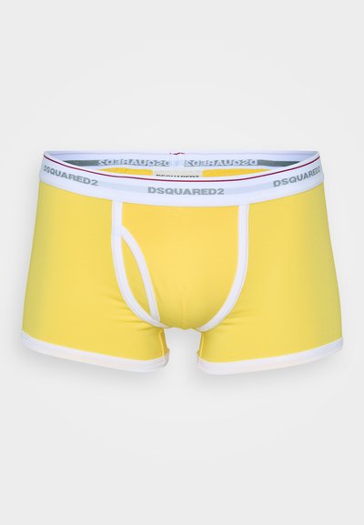 Gula boxershorts med en tight passform, vit kant, och en midjeresår med märket "DSQUARED2" i grå text.