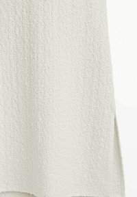 Tissu blanc texturé avec une surface douce et légèrement rugueuse. Présente des fentes sur les côtés pour faciliter le mouvement et un design simple et sans ornements.