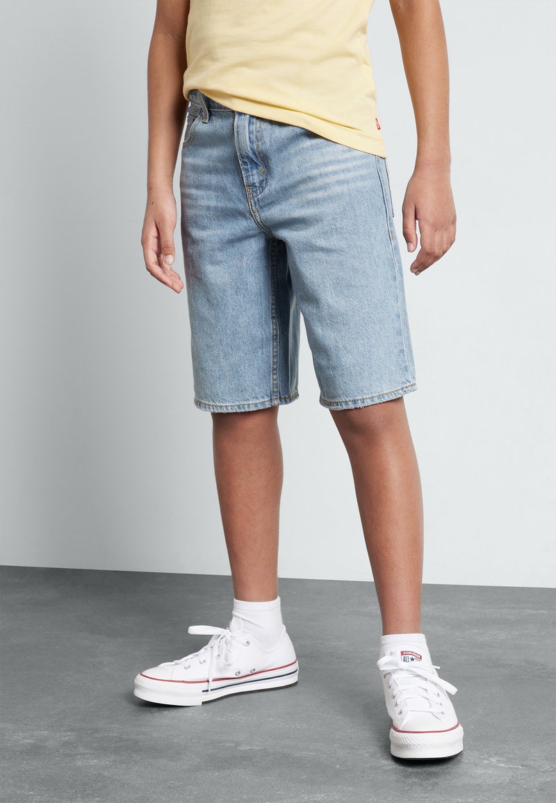Lyseblå denim shorts med regular fit, frynset kant, sidelommer, slidt stof, parret med hvide høj-top sneakers og sokker.