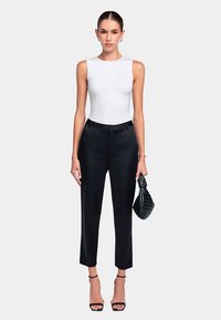 Body sans manches blanc associé à un pantalon noir sur mesure, doté d'une coupe fuselée et classique, complété par un sac à main noir structuré.
