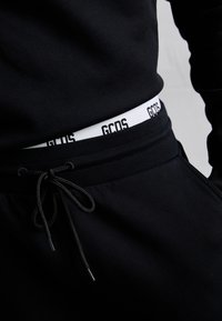 Czarna bluza i spodnie dresowe ze sznurkiem; posiadają biały pas z napisem "GCOS" w czerni. Materiał o fakturze, dopasowany krój.