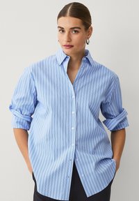 Hellblaues Button-up-Hemd mit weißen und dunkleren blauen Streifen. Verfügt über einen spitzen Kragen, hochgeknöpfte Ärmel und eine lockere Passform.