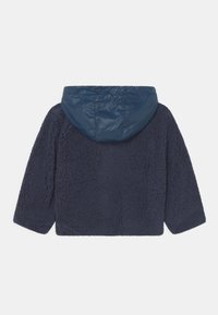 Casaco de fleece azul marinho com um corpo macio e texturizado e um capuz liso e brilhante. Apresenta mangas largas e uma silhueta rectangular.