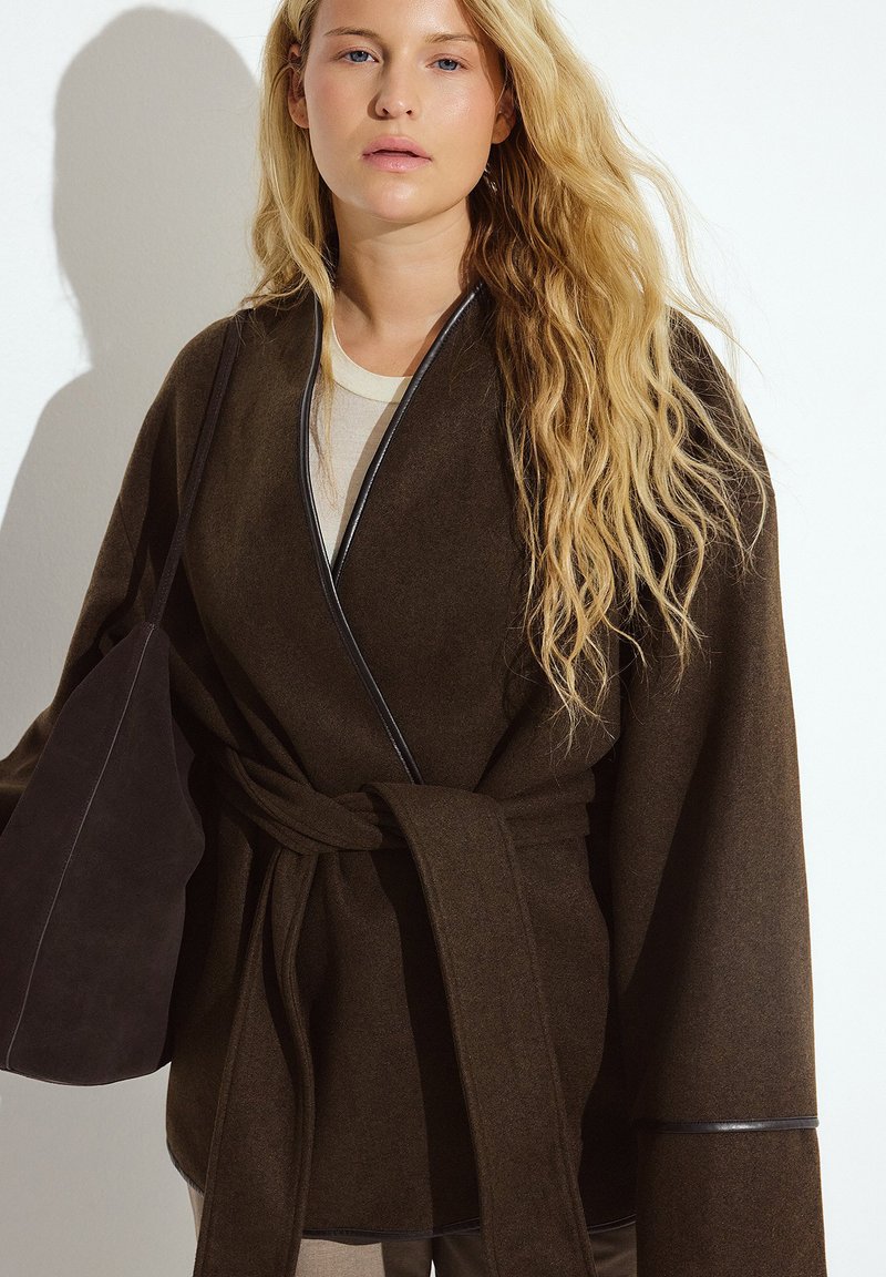 Dunkelbrauner Wollkimono im Wrap-Stil mit weiten Ärmeln, tailliert mit einem Gürtel und schwarzen Paspeln entlang der Kanten.
