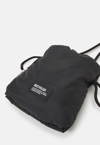 Czarna, miękka torba na sznurku z etykietą "RECYCLED", podkreślającą wykorzystanie materiałów ekologicznych, na białym tle.