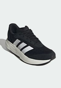 Czarny but sportowy z tekstylną cholewką, z trzema białymi paskami po bokach, białą amortyzowaną midsole oraz czarną gumową podeszwą.