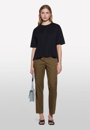 T-shirt noir oversize, pantalon slim fit vert olive, et sandales noires ouvertes. Sac à bandoulière bleu clair avec une sangle. Textures de tissu lisses.