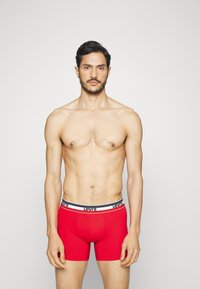 Piros pamut boxer alsónadrág fekete-fehér elasztikus derékpánttal, amelyen a "Levi's" logó látható. A modellen felső nélkül, egyenesen állva látható.